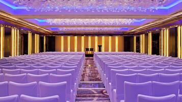 A conference room with rows of white chairs, a podium at the front, and a ceiling with a decorative light fixture.