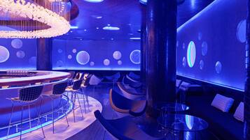 A modern lounge area with a bar, seating, and a unique ceiling design featuring hanging lights and illuminated spheres.