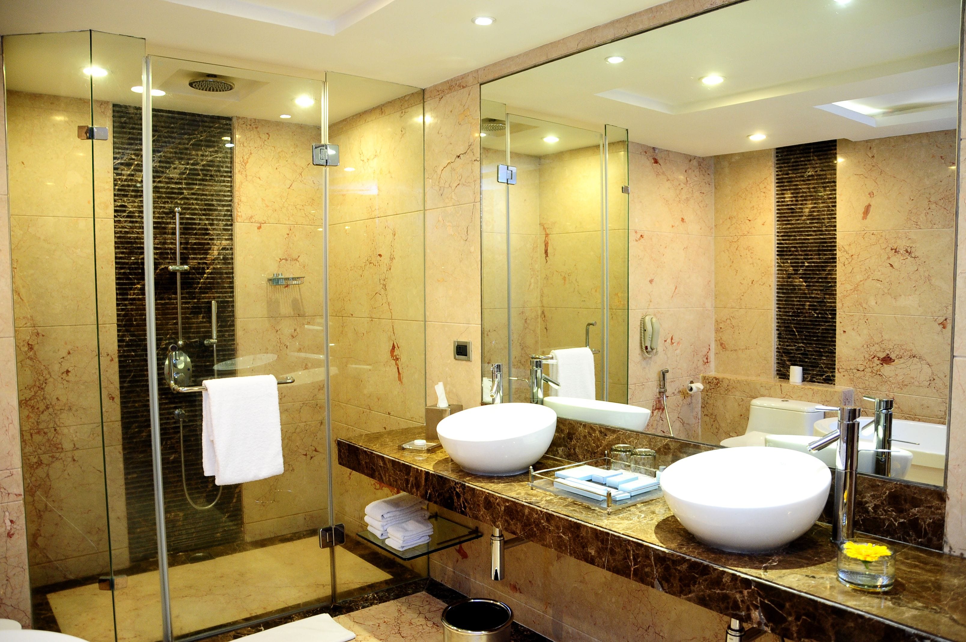 Un baño moderno con ducha envuelta en vidrio, dos lavamanos y un espejo grande.