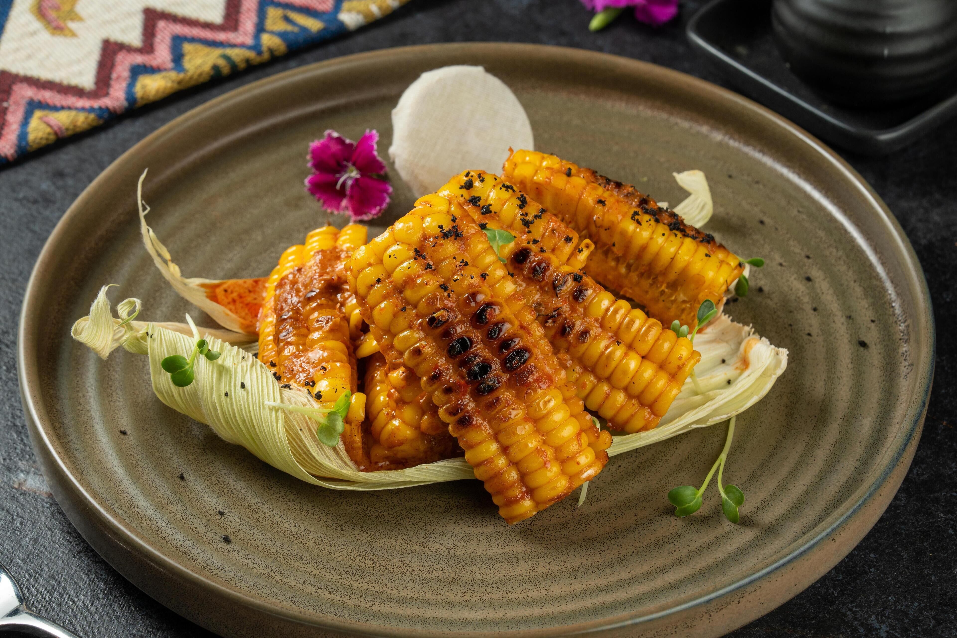 Grilled corn on the cob with a creamy dip, garnished with herbs, on a ceramic plate.