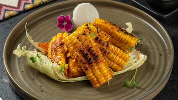 Grilled corn on the cob with a creamy dip, garnished with herbs, on a ceramic plate.