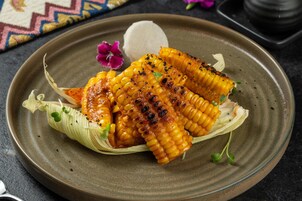 Grilled corn on the cob with a creamy dip, garnished with herbs, on a ceramic plate.