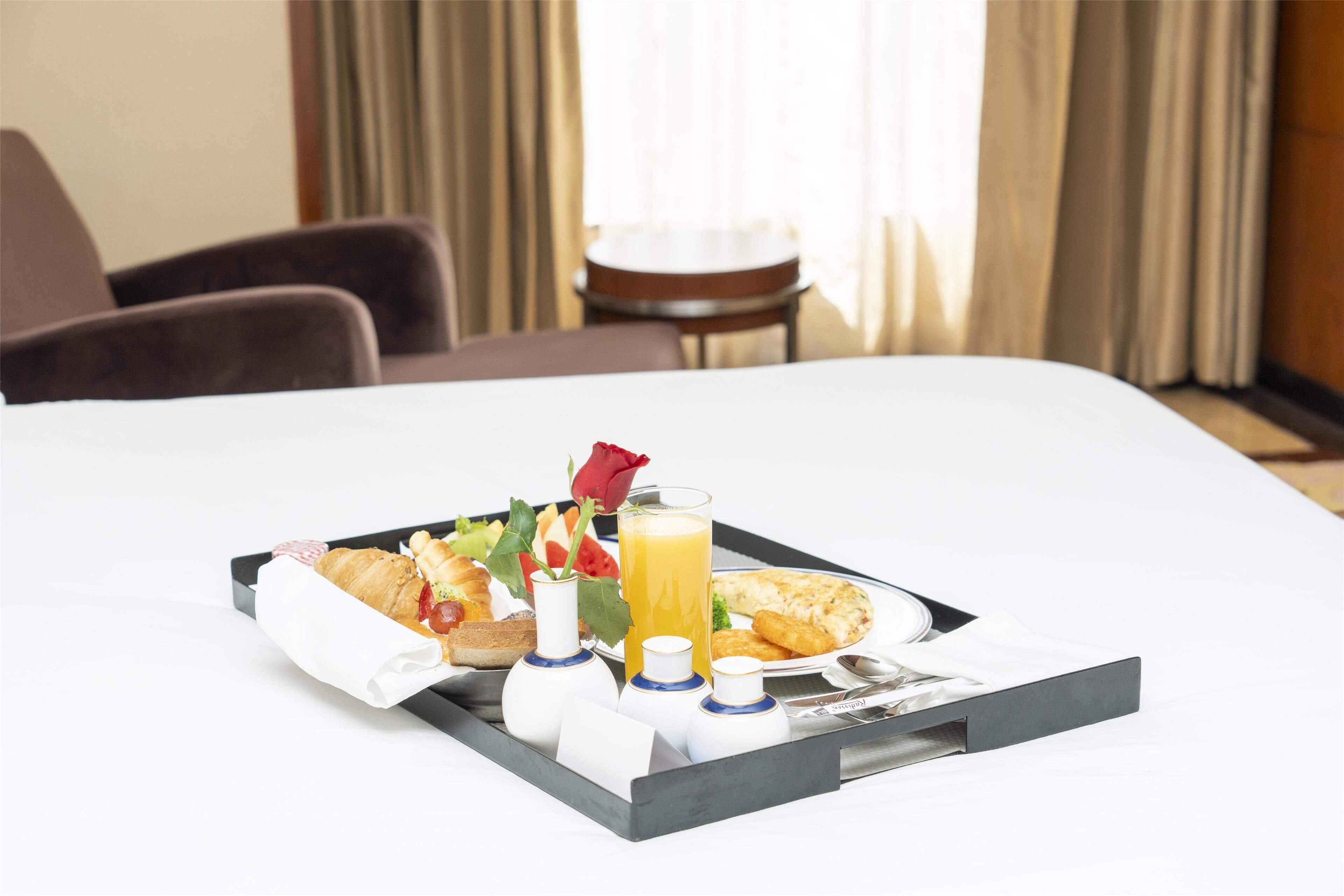 En välordnad frukostbricka står på sängen i hotellrummet, med croissanter, ett glas apelsinjuice och en ros.