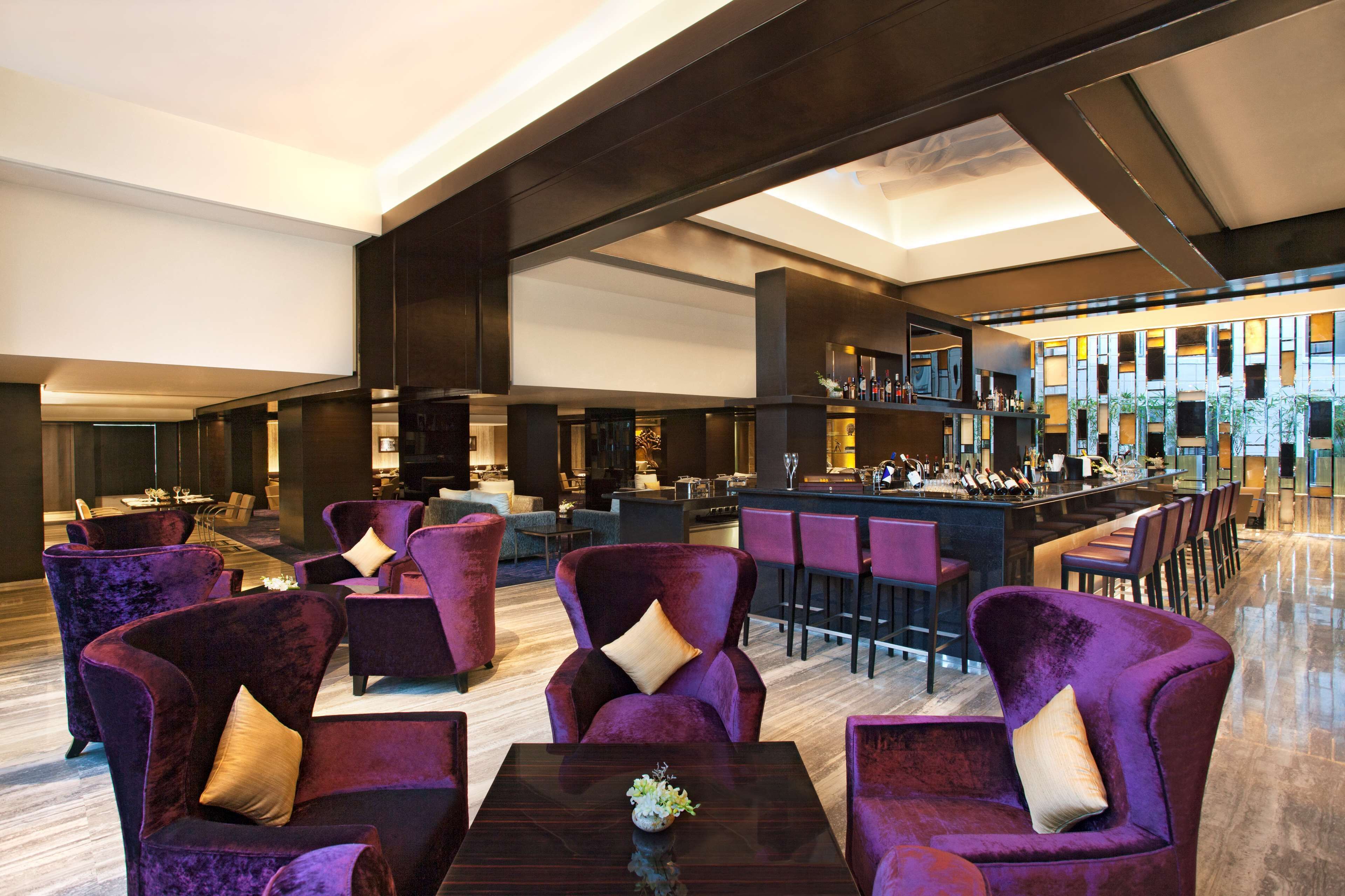 Un hall d’entrée spacieux avec des fauteuils violets, un coin bar et, au fond, une cuisine moderne.