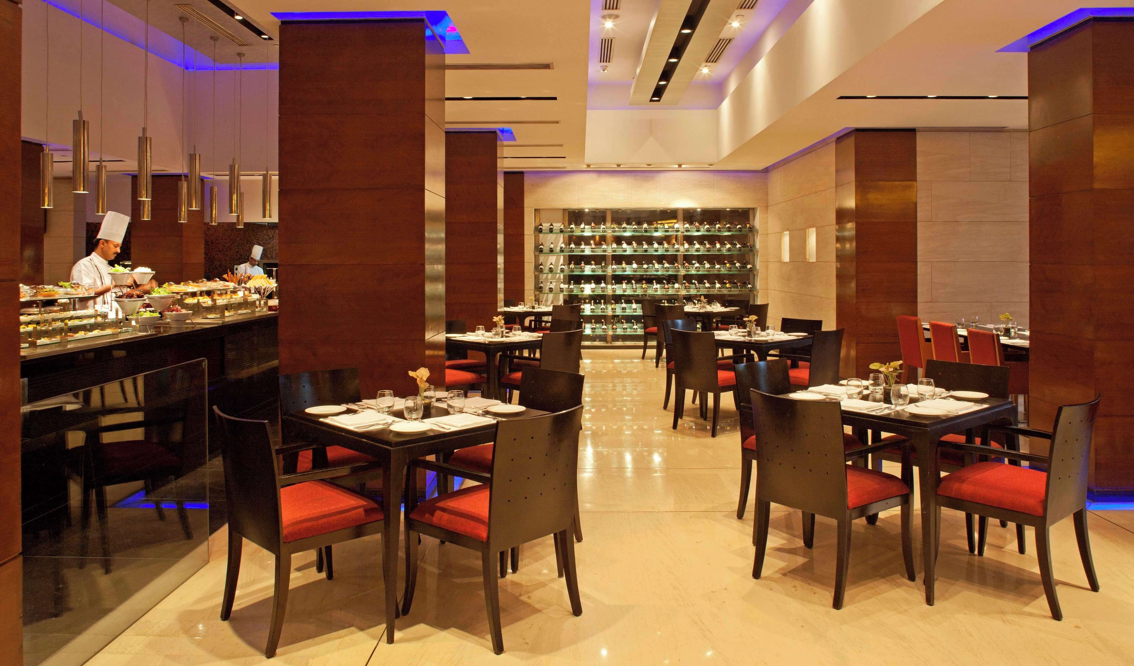 A restaurant with a bar area, multiple dining tables, and red cushioned chairs.