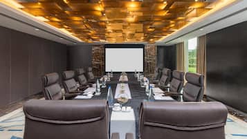 Un salón de conferencias con una larga mesa, sillas de cuero y una pantalla para proyector.