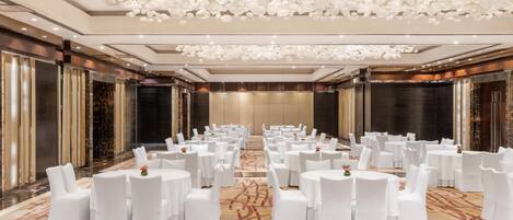 A banquet hall with round tables and white chairs, a patterned carpet, and a decorative ceiling.