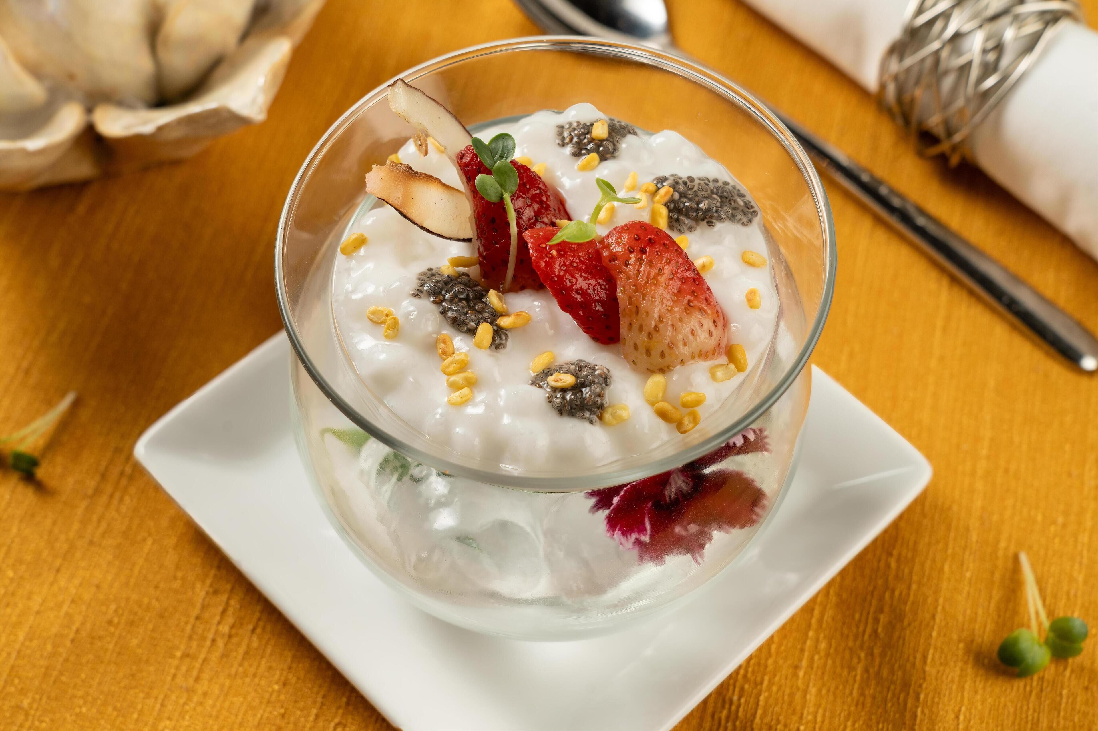 A bowl of yogurt topped with strawberries, chia seeds, and a slice of kiwi on a white plate.