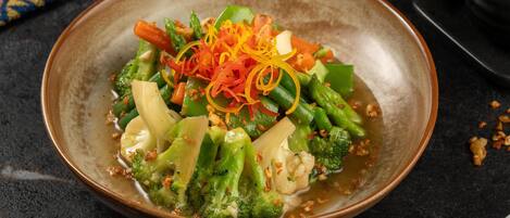 Un bol de légumes sautés, agrémentés de carottes râpées et d’oignons verts, servi dans un bol en céramique sur une surface sombre.