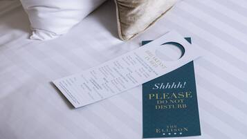 A hotel room with a neatly made bed, a pillow, and a sign that reads "Please do not disturb."