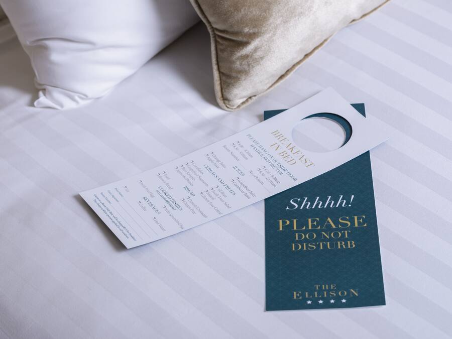 A hotel room with a neatly made bed, a pillow, and a sign that reads "Please do not disturb."