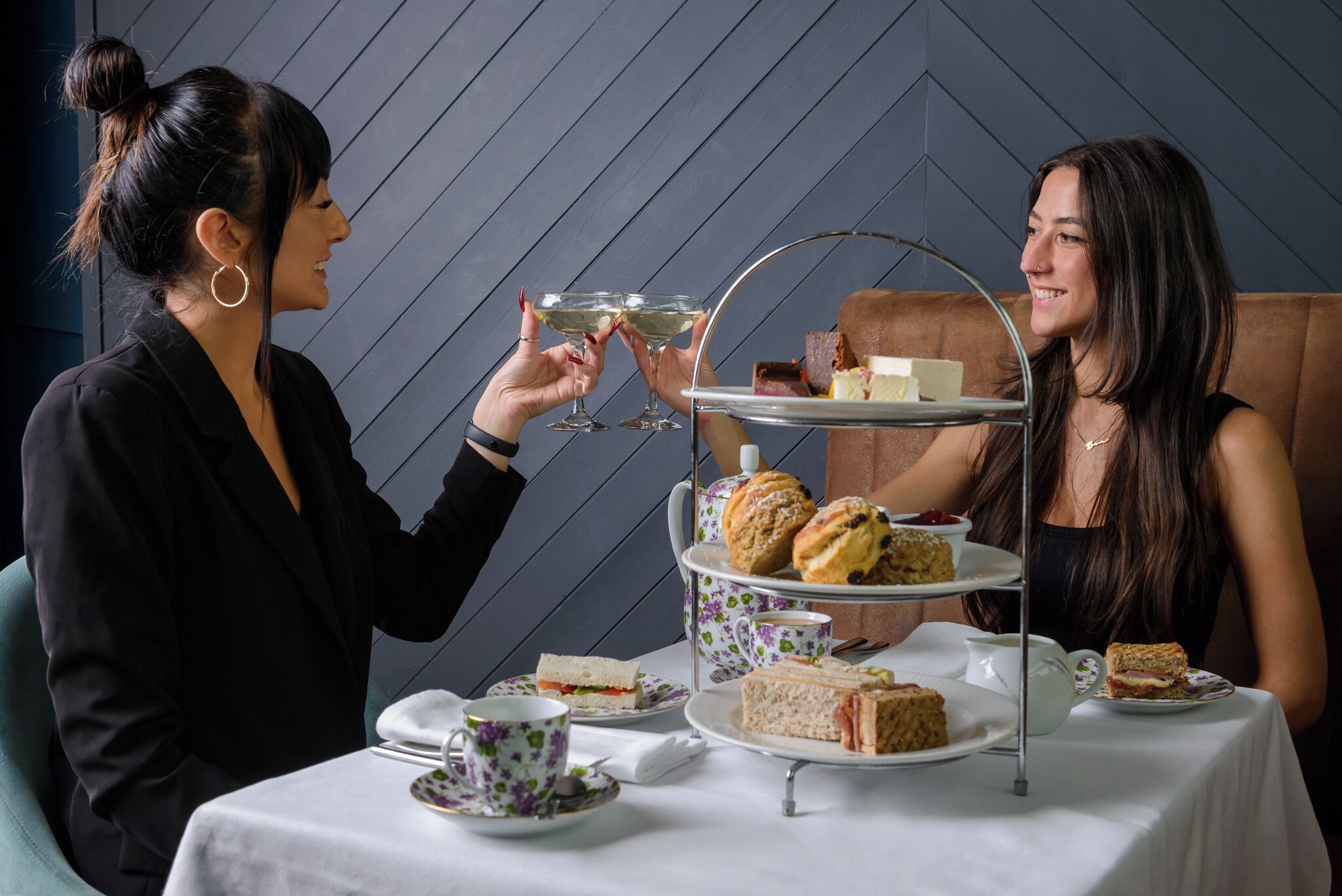 Una mesa dispuesta para un servicio de té, con un soporte de varios niveles que contiene sándwiches y scones, y una taza de té sobre la mesa.