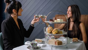 Ett bord dukat för en tebjudning med ett våningsfat som innehåller smörgåsar och scones, och en kopp te på bordet.