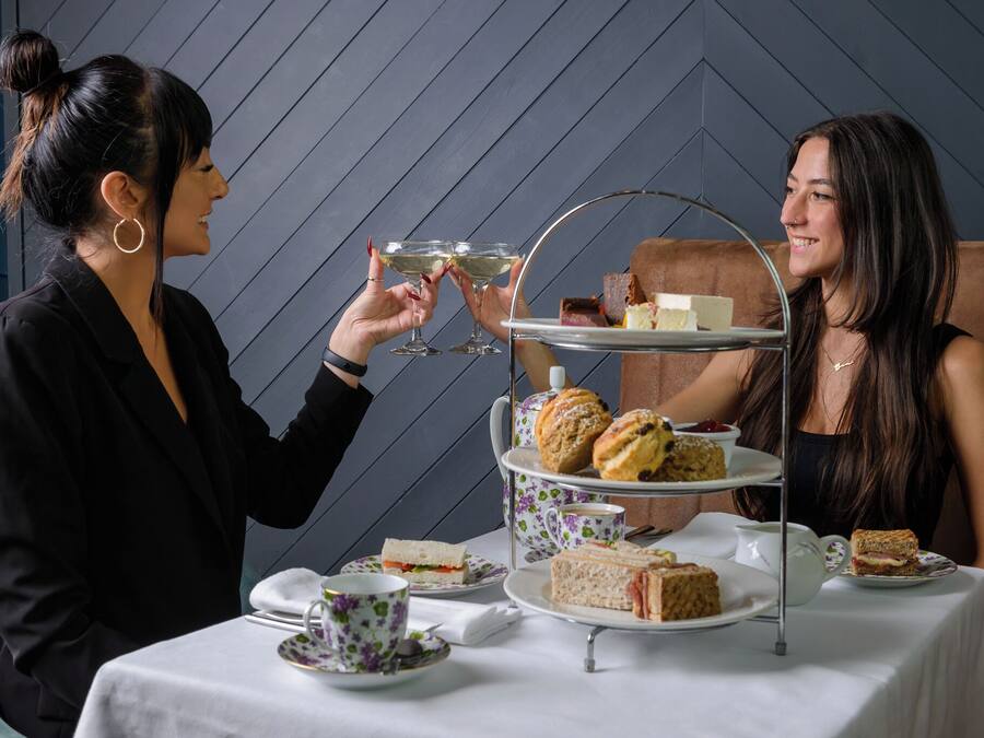 Ett bord dukat för en tebjudning med ett våningsfat som innehåller smörgåsar och scones, och en kopp te på bordet.