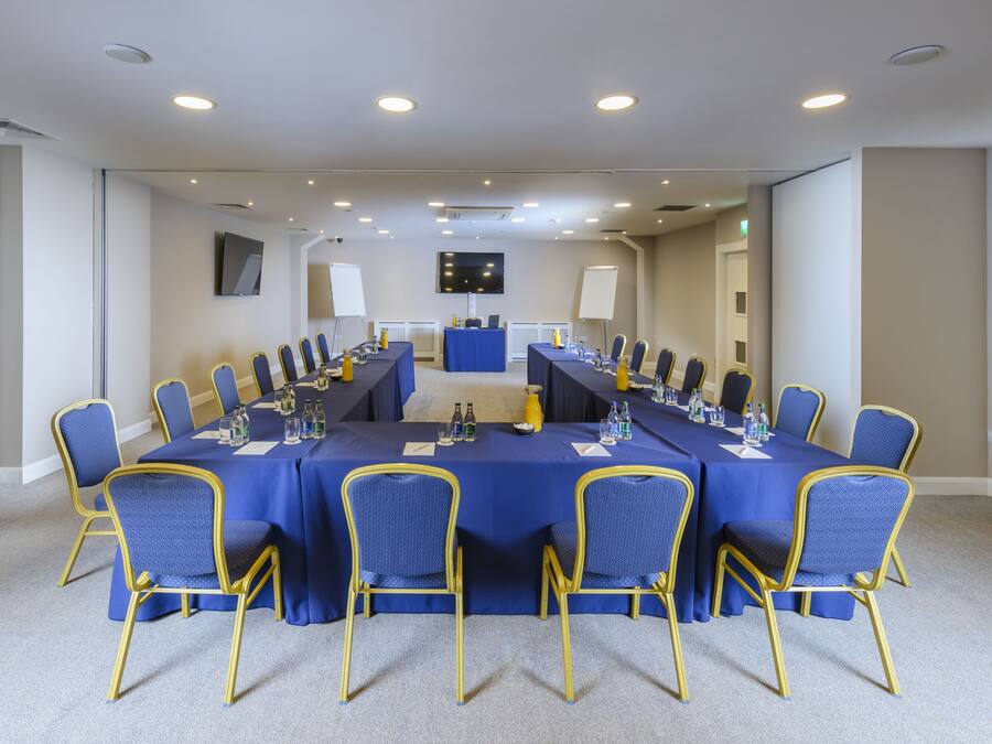 A conference room with a long table, blue chairs, and a television screen.