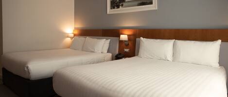 Two single beds with white linens, a wooden headboard, bedside lamps, and a framed picture on the wall.