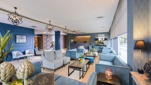 A modern lounge area with blue sofas, a coffee table, and decorative art pieces. - The Ellison Hotel (Castlebar)