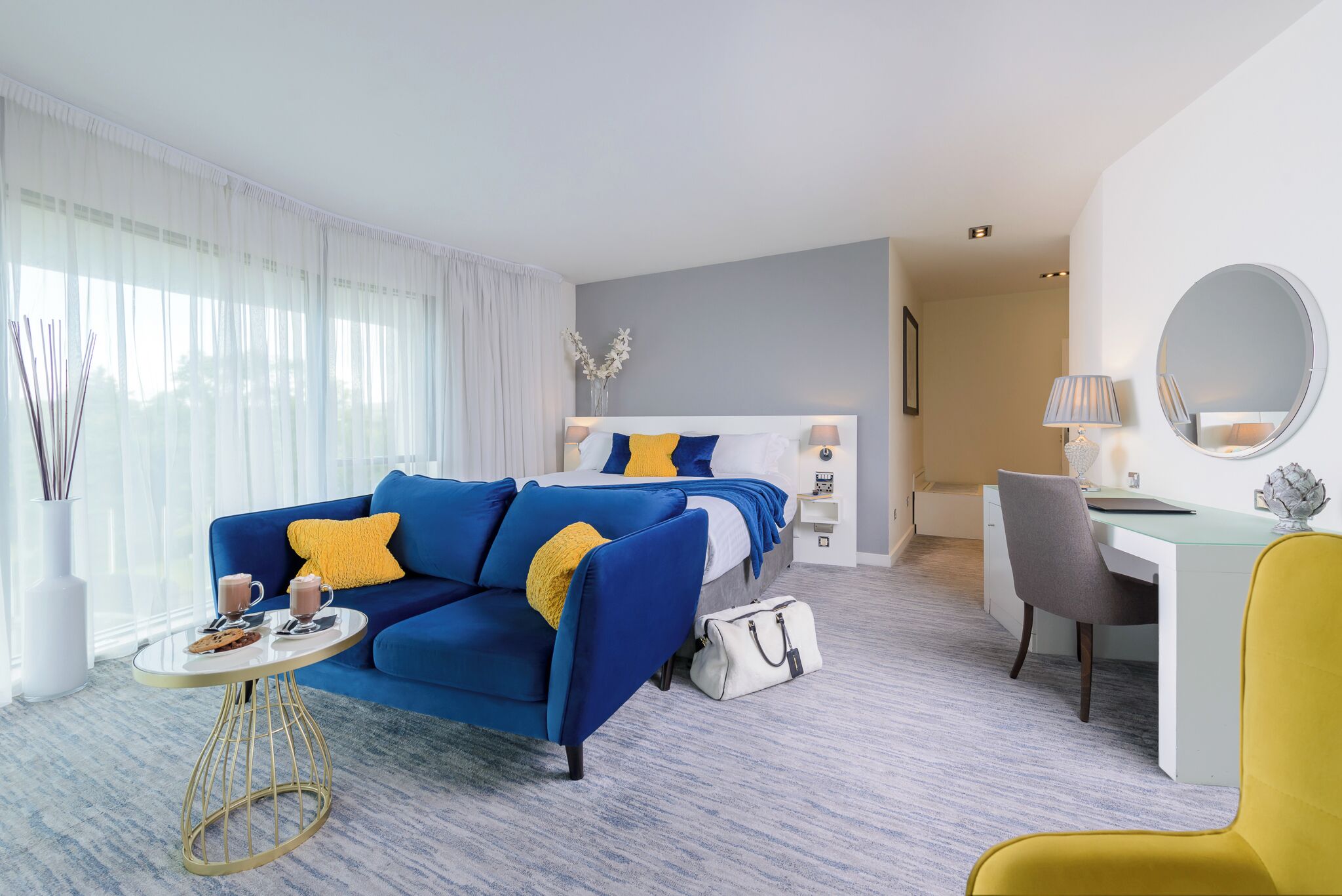 A hotel room with a bed, a blue sofa, a desk, and a chair.