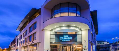 A modern hotel with a curved facade, a prominent entrance, and a neon sign for 'The Ellison'.
