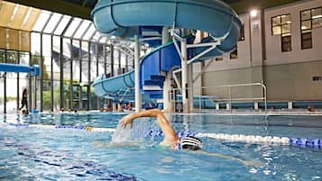 Una piscina con carriles, un tobogán acuático y una persona nadando.