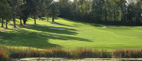 Un campo de golf con un estanque, árboles y cielo despejado.