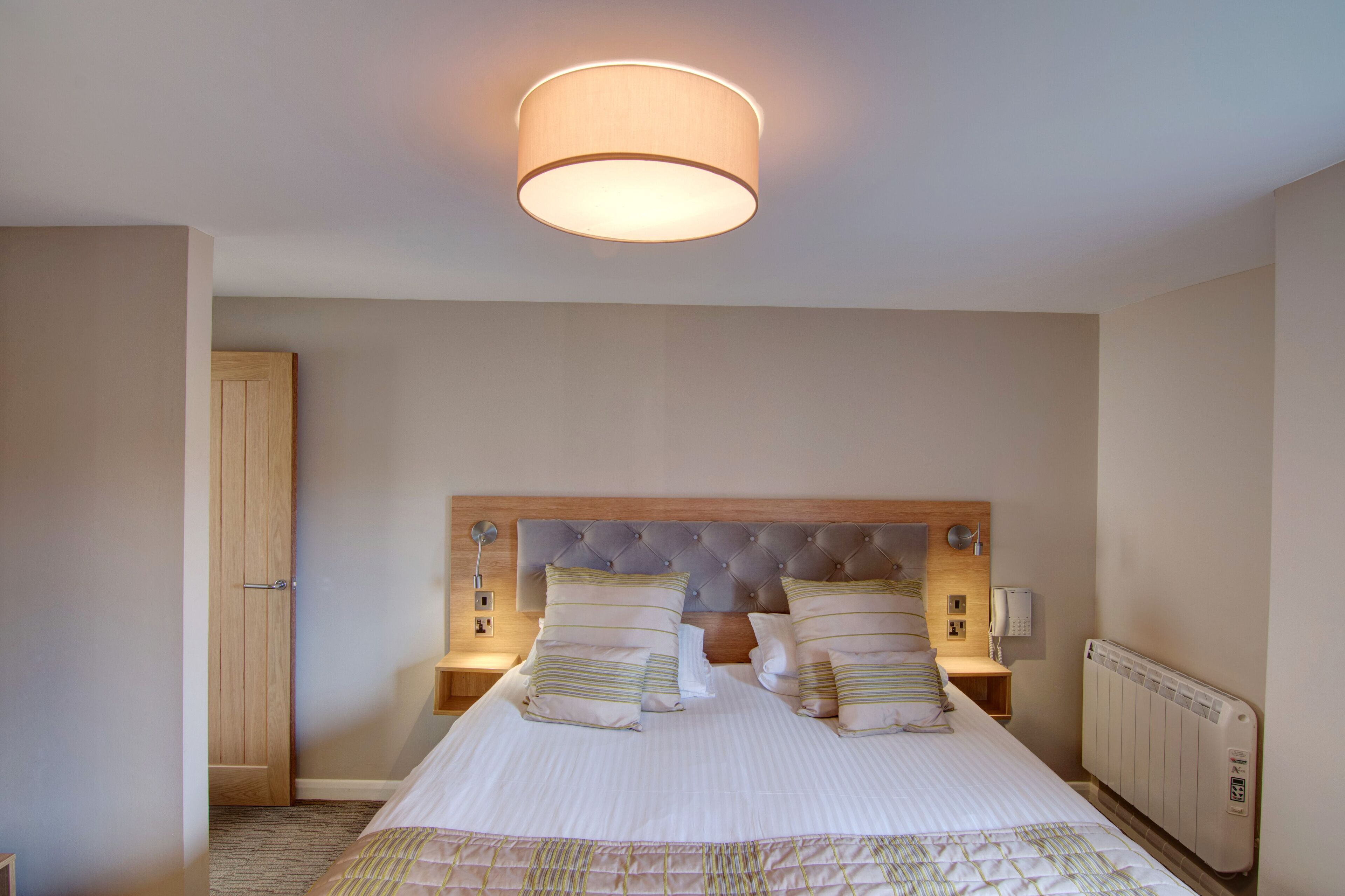 Un dormitorio ordenado con una cama grande, dos mesitas de noche, un cabecero de madera y una lámpara en el techo.