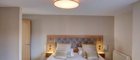 A neatly arranged bedroom with a large bed, two bedside tables, a wooden headboard, and a ceiling light fixture.
