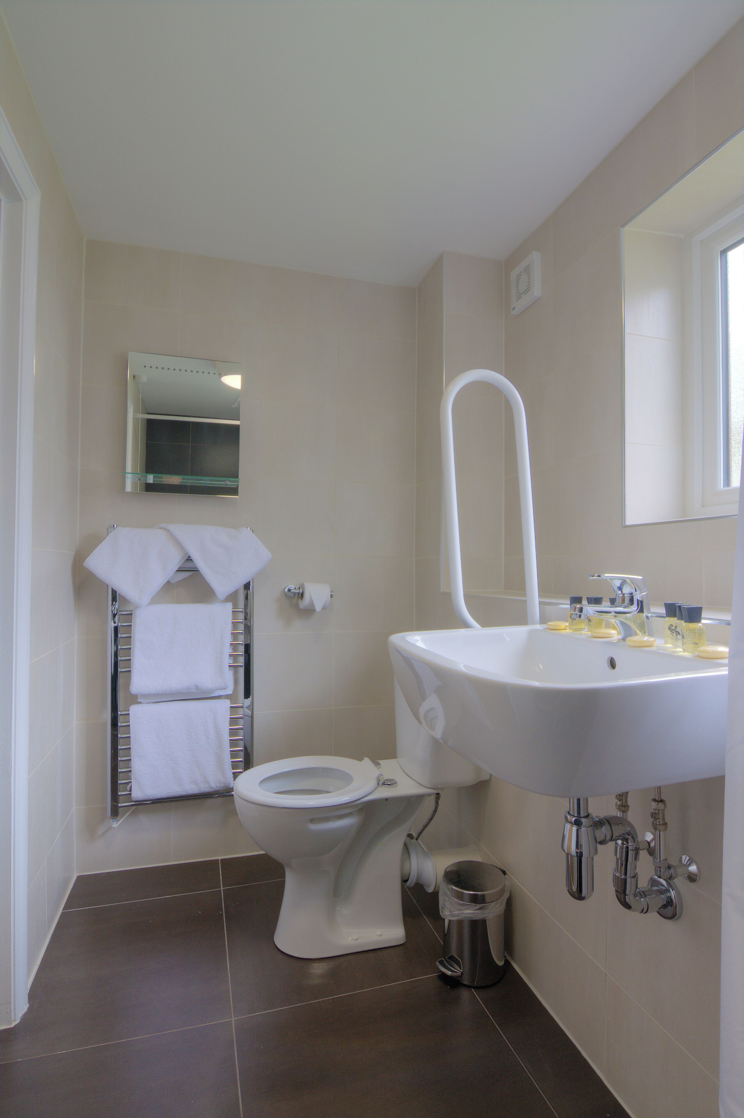 A bathroom with a white sink, a toilet, a towel rack with towels, a mirror, and a trash can.