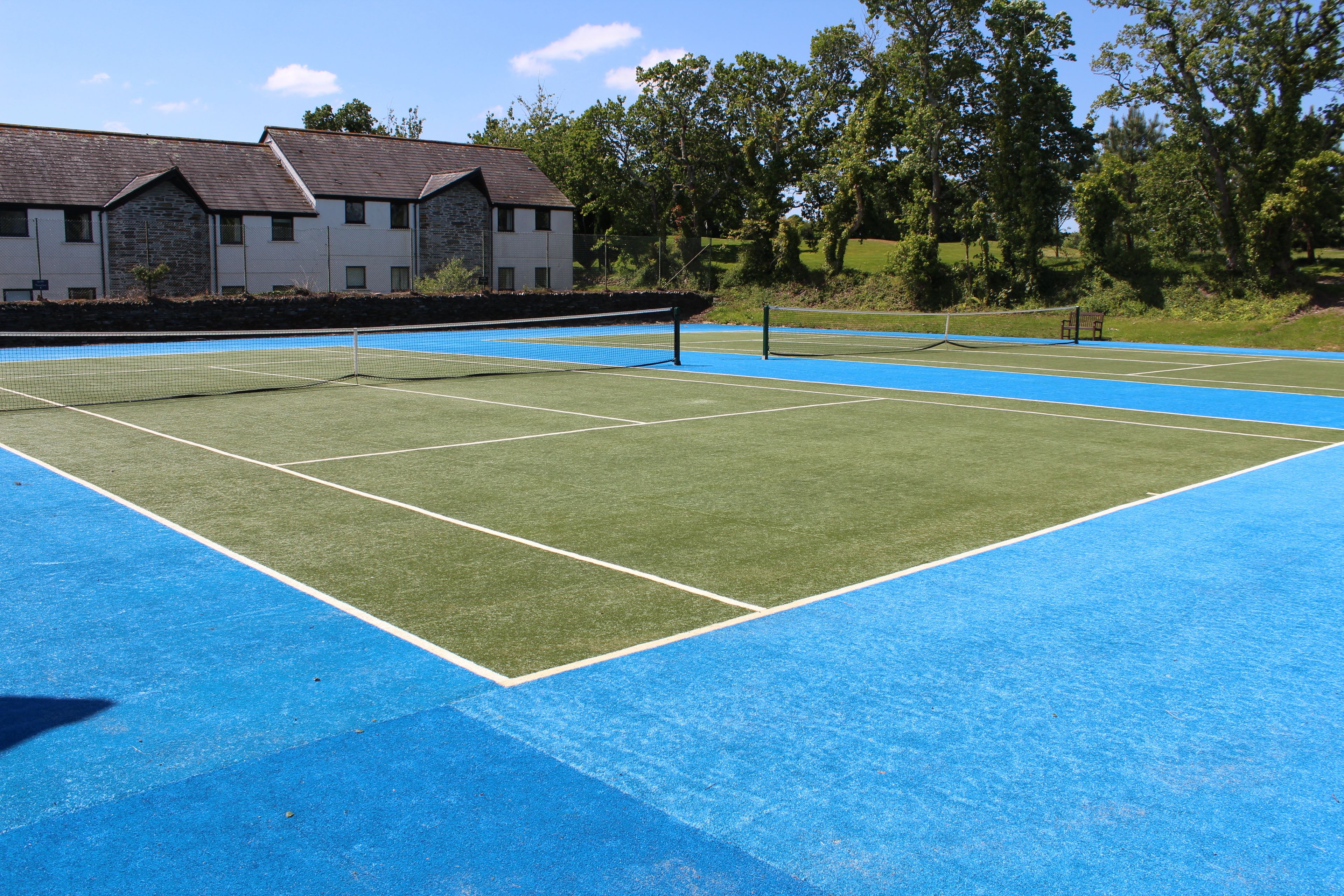 A tennis court with a net, surrounded by a blue surface and green grass.