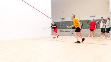 A squash court with players in motion, a net, and a wall with a clock.