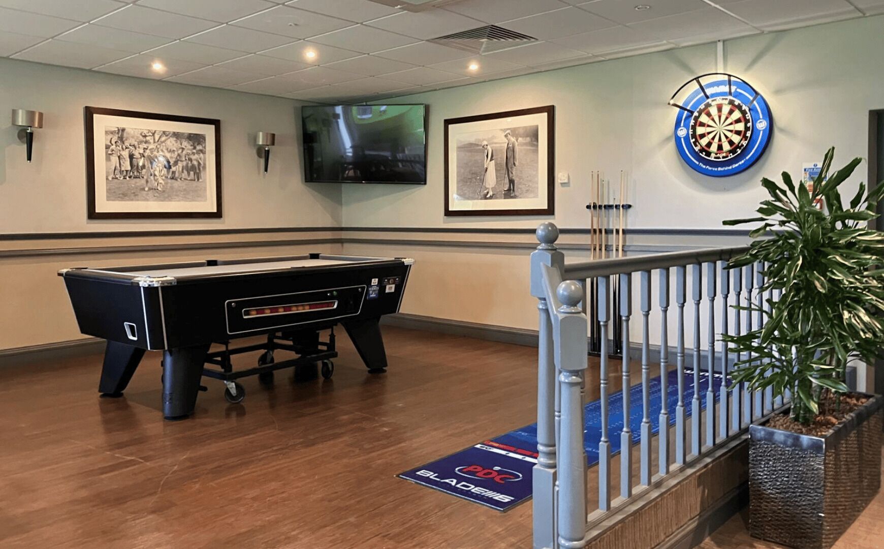 A billiards room with a pool table, a dartboard, and framed photographs on the walls.