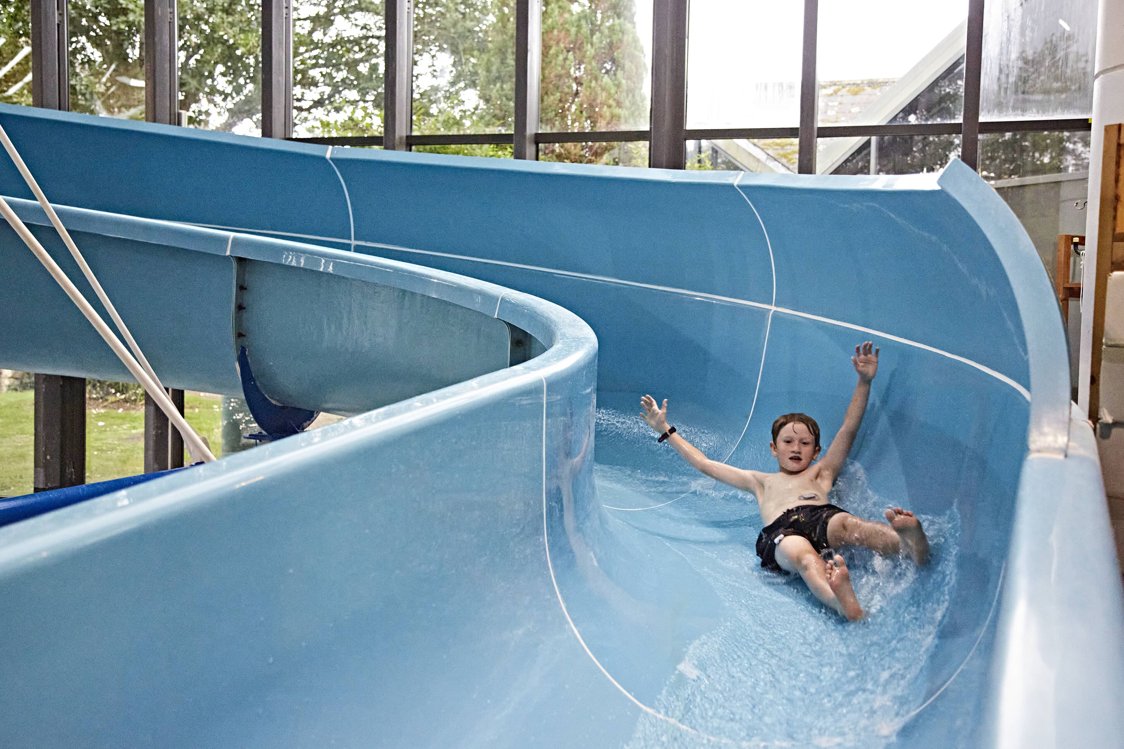 Un enfant glisse sur un toboggan aquatique bleu à l’intérieur d’un parc aquatique couvert.