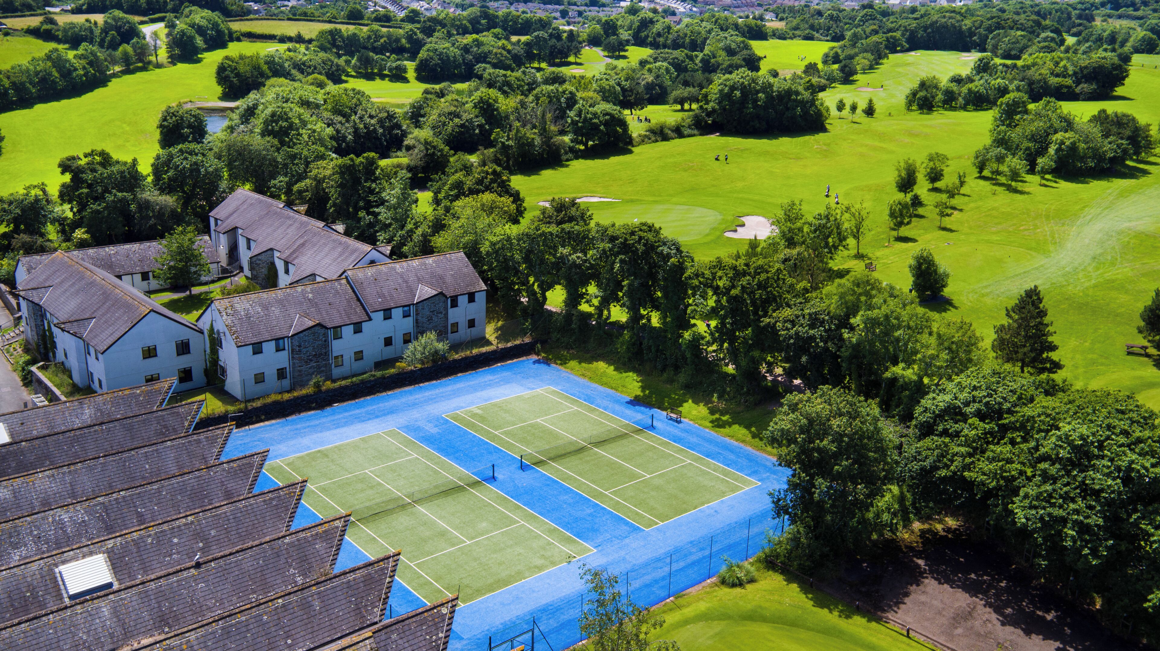A large building with a tennis court and a golf course in the background.