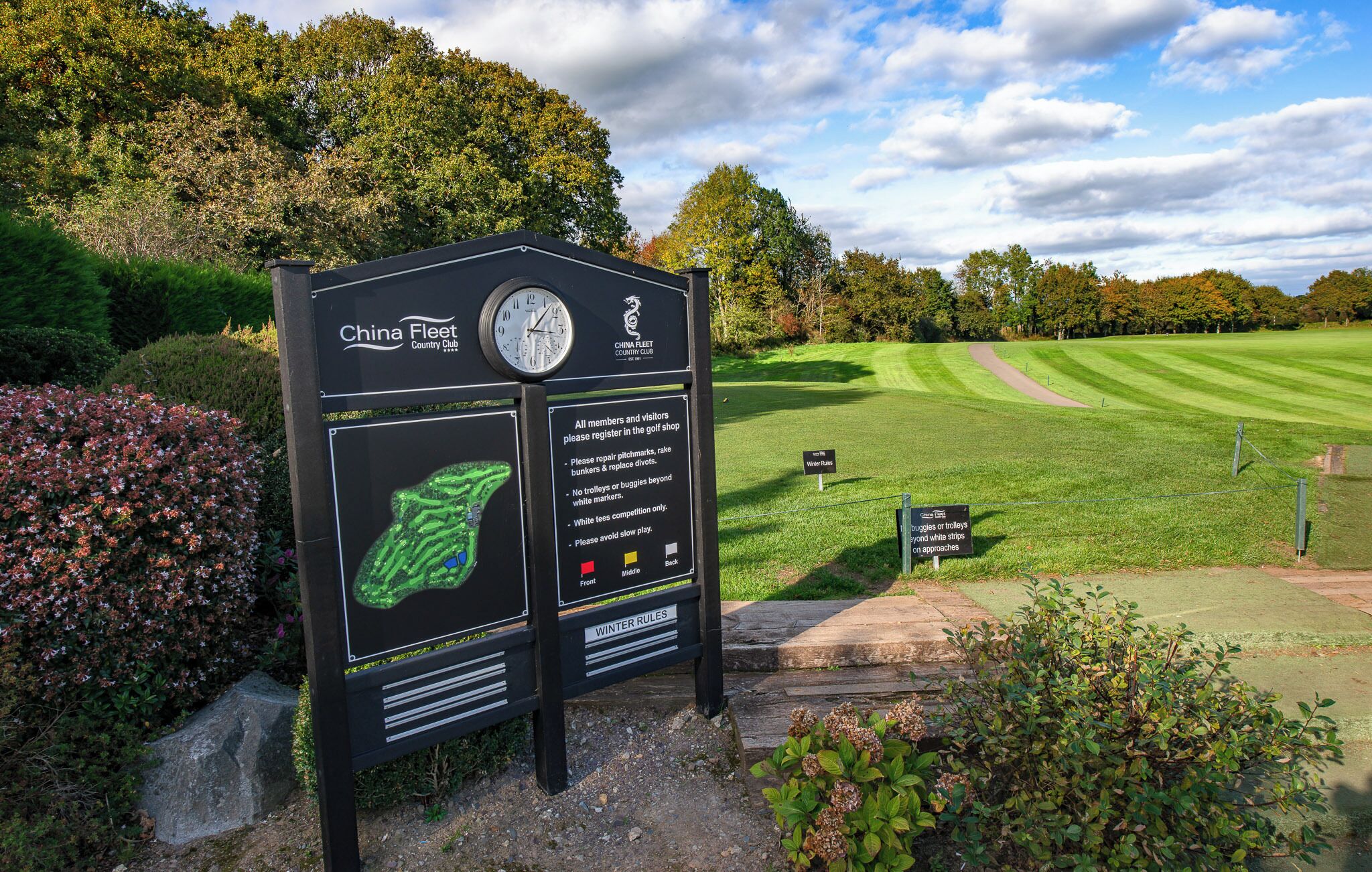 A golf course sign with rules and a clock.