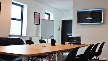 A conference room with a long table, black chairs, a whiteboard, a laptop, and a screen displaying a website.