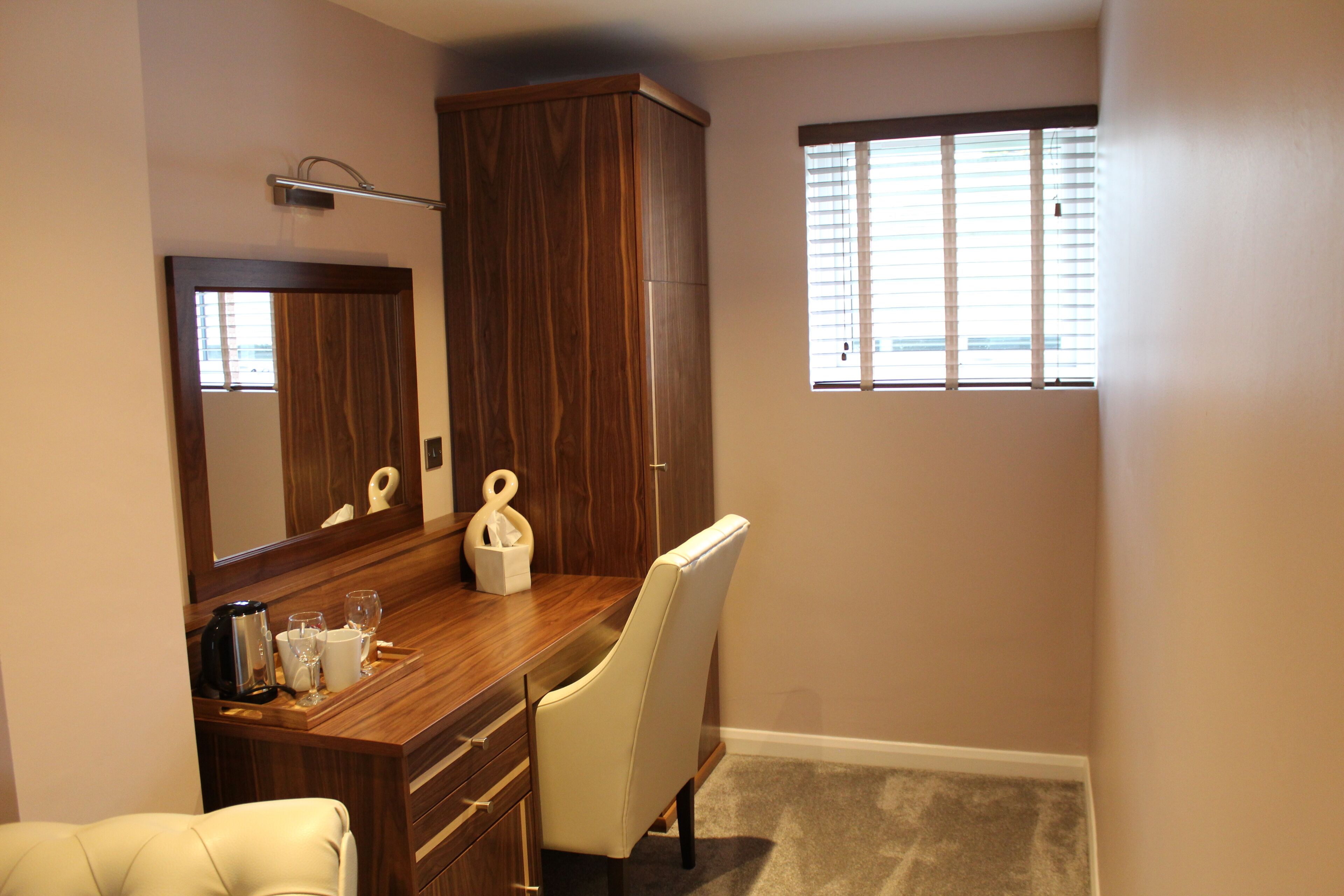 A bathroom with a wooden vanity, a mirror, a chair, and a window with blinds.