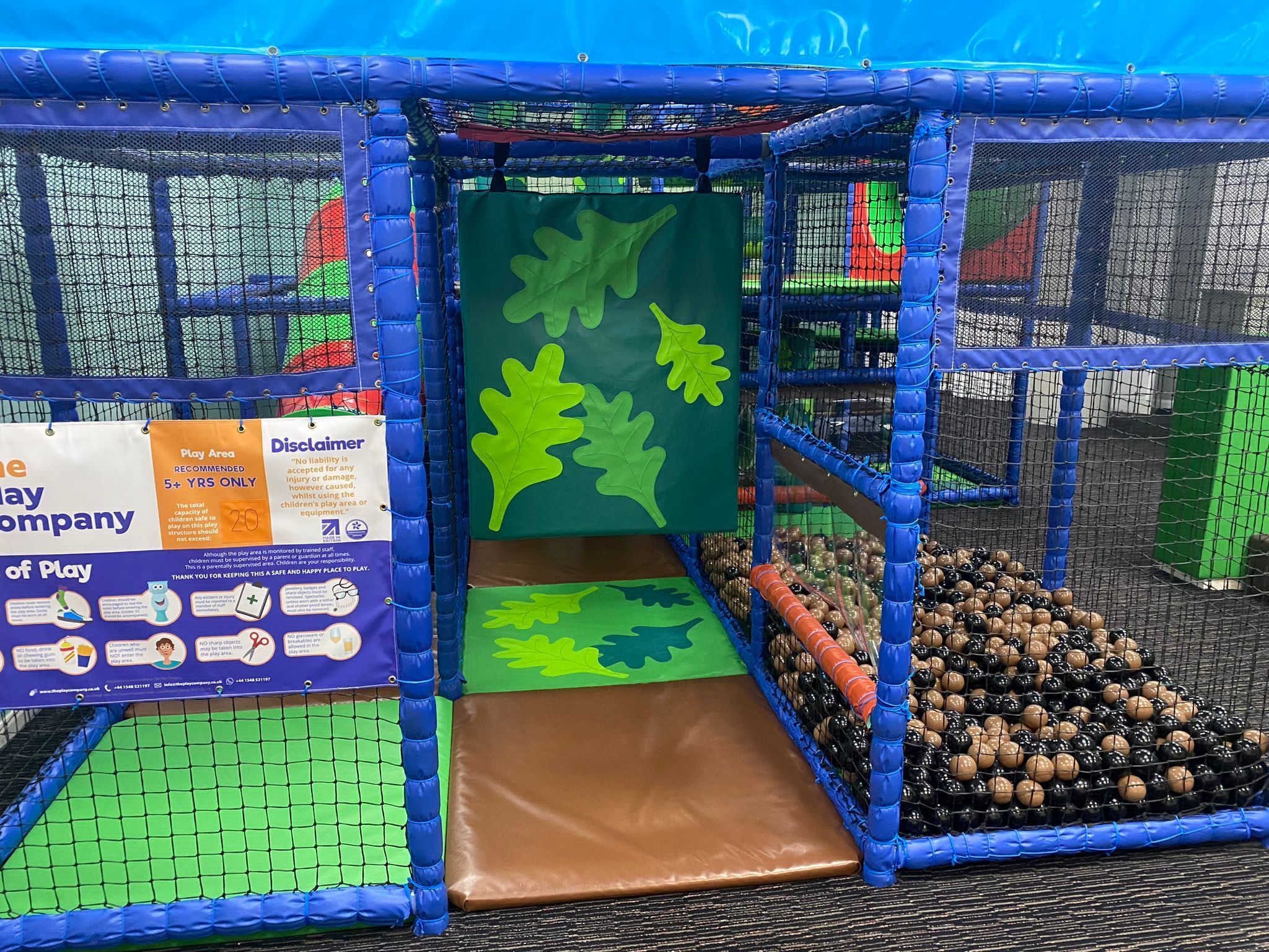 A play area with a netted enclosure, a slide, and a play mat with leaf designs.
