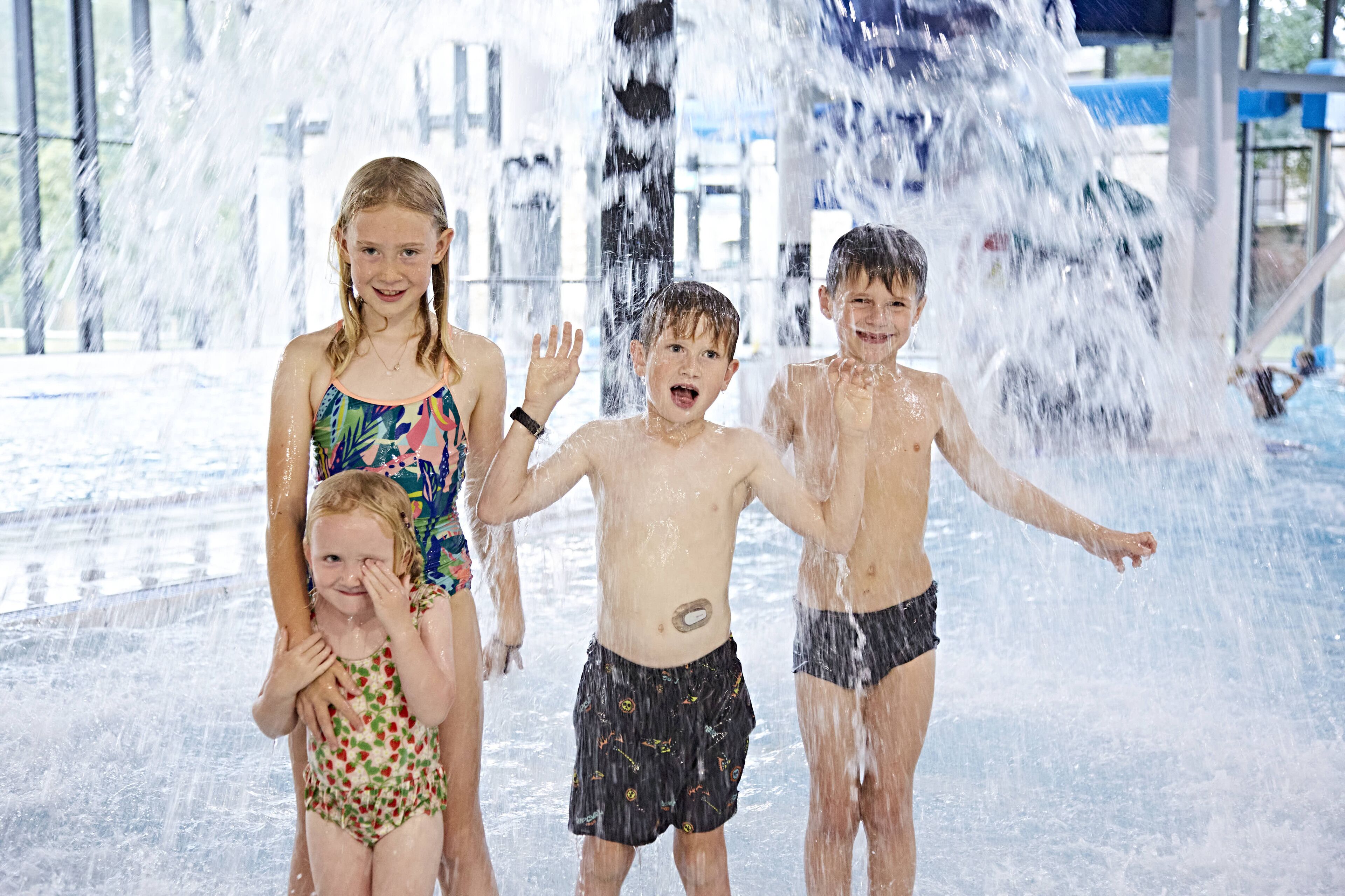 A group of children playing in a water feature with a large glass enclosure.
