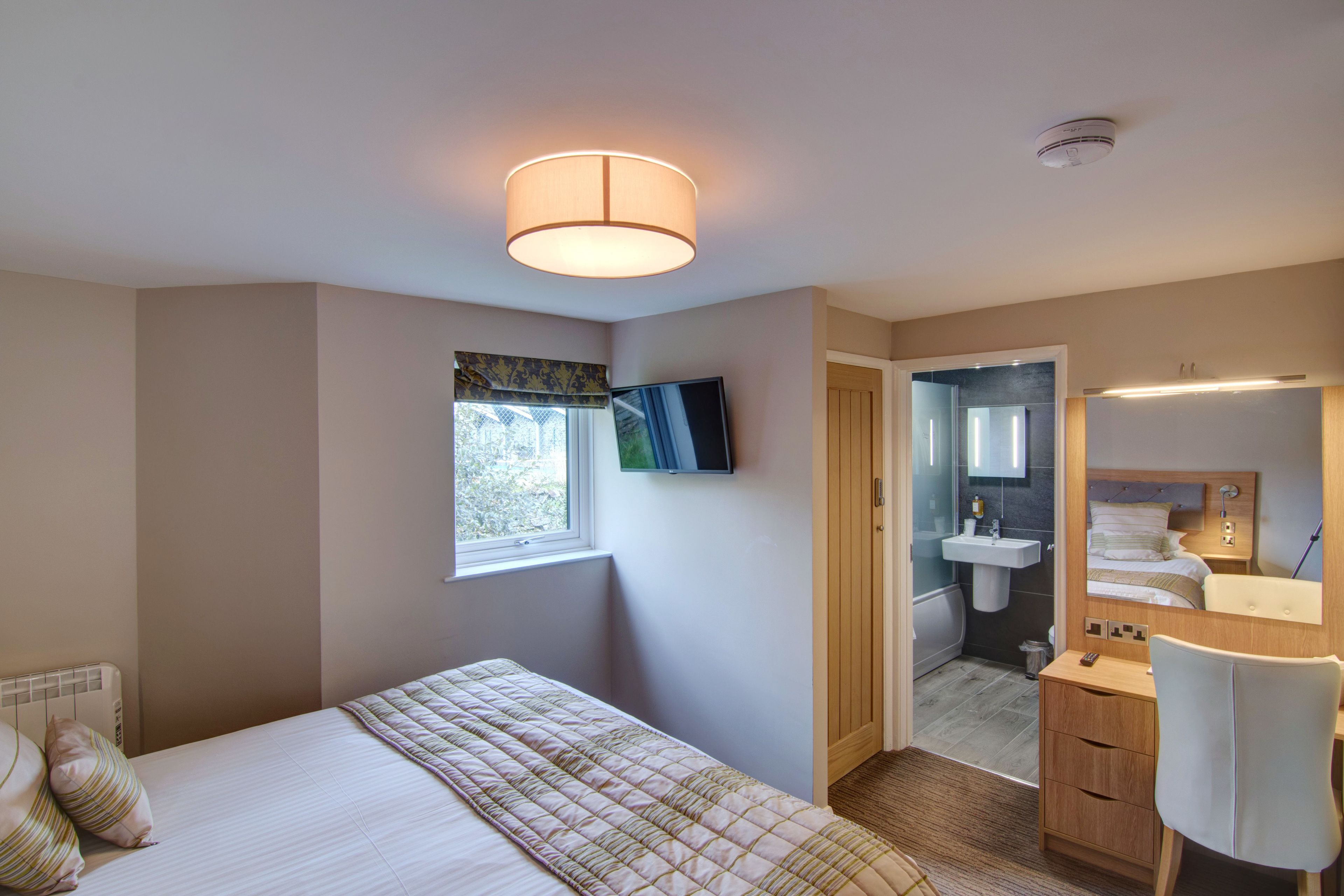 A bedroom with a bed, a desk, a mirror, a TV, and a bathroom with a sink and toilet.