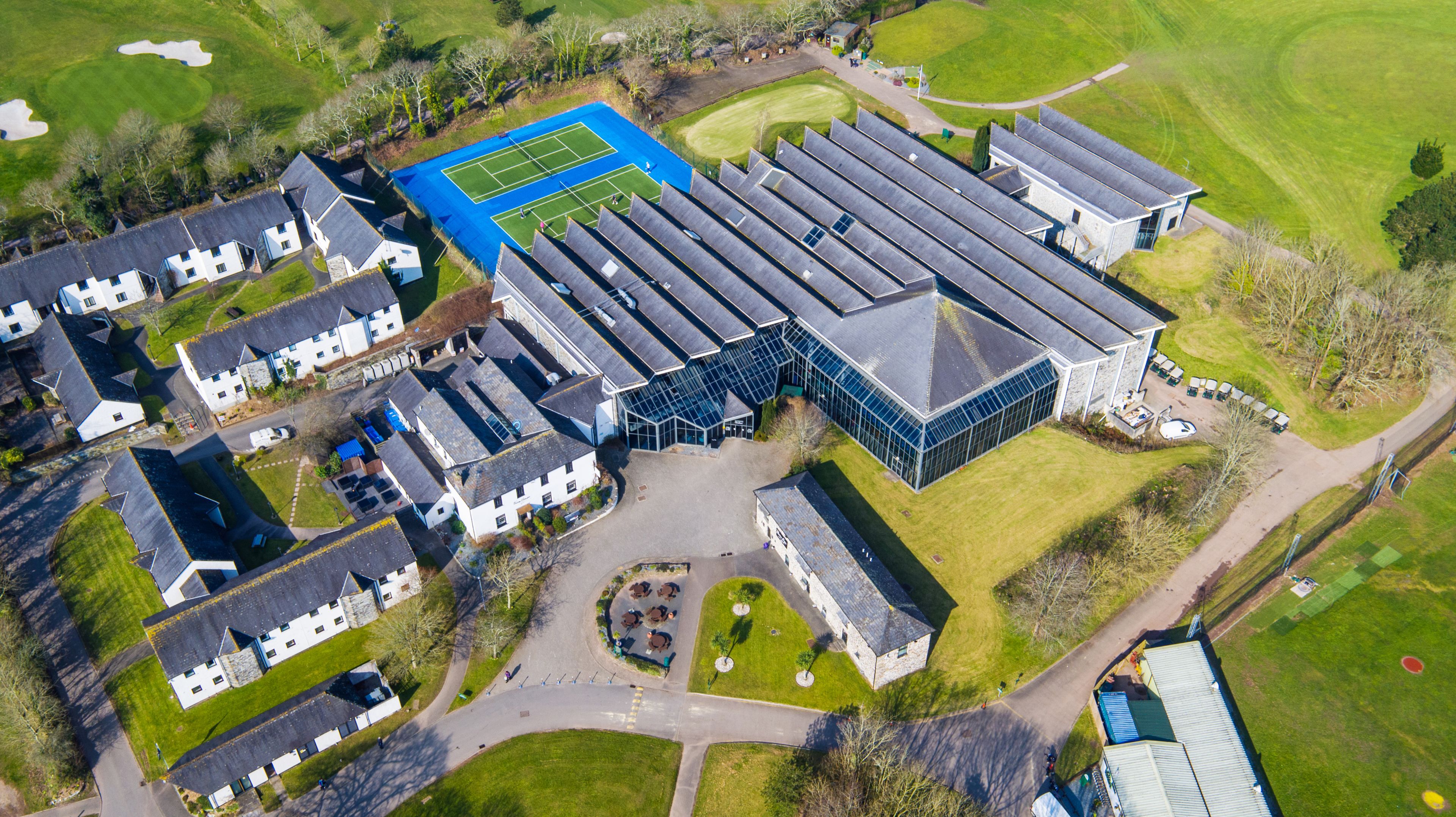An aerial view of a residential area with houses, a tennis court, and a large building with a modern design.