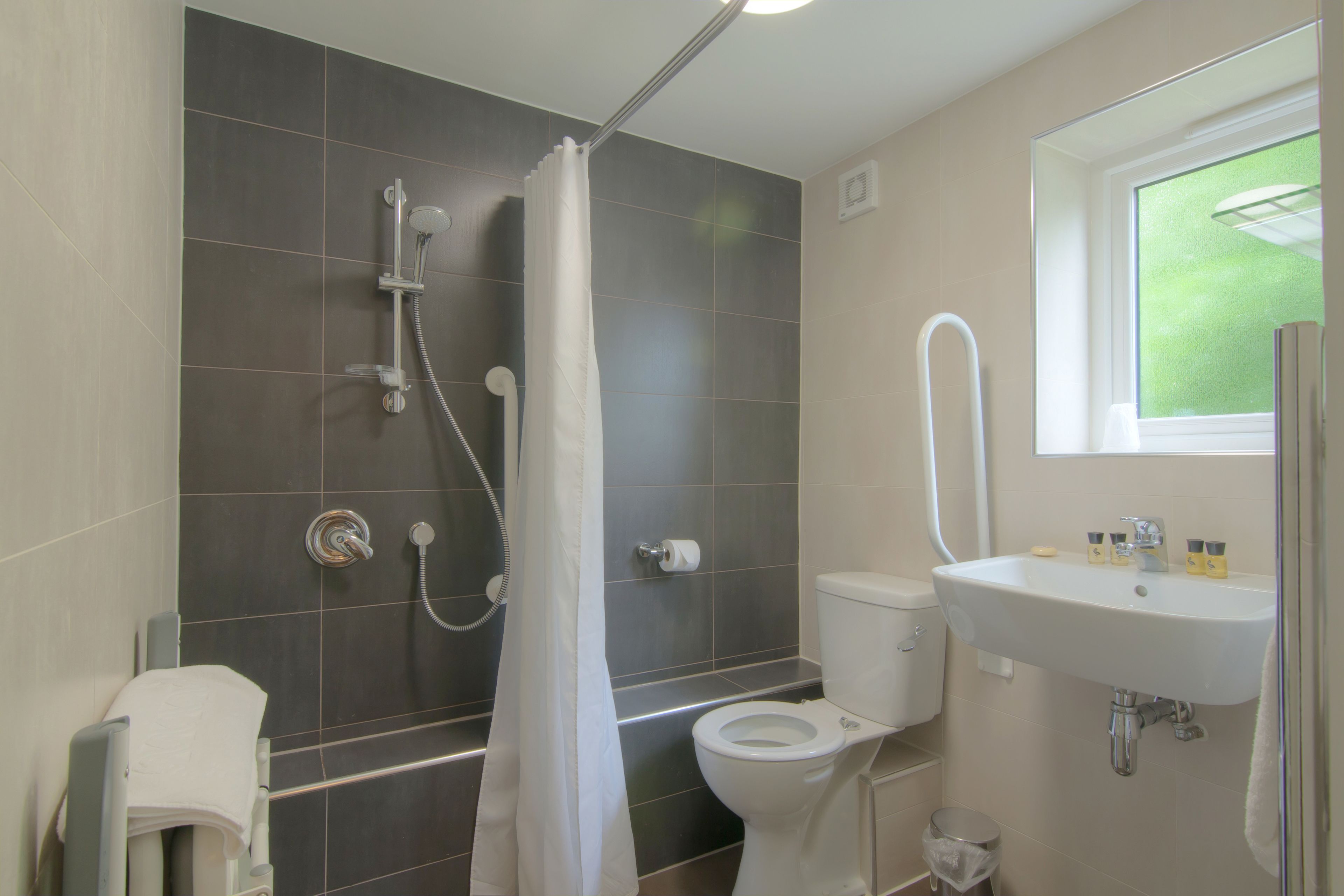 A bathroom with a shower, toilet, sink, and a window.