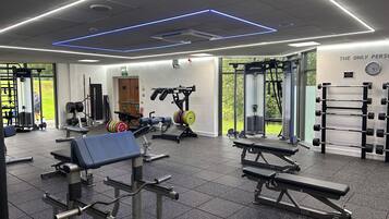A modern gym with various exercise equipment, including benches and weight machines, and a wall-mounted squat rack.