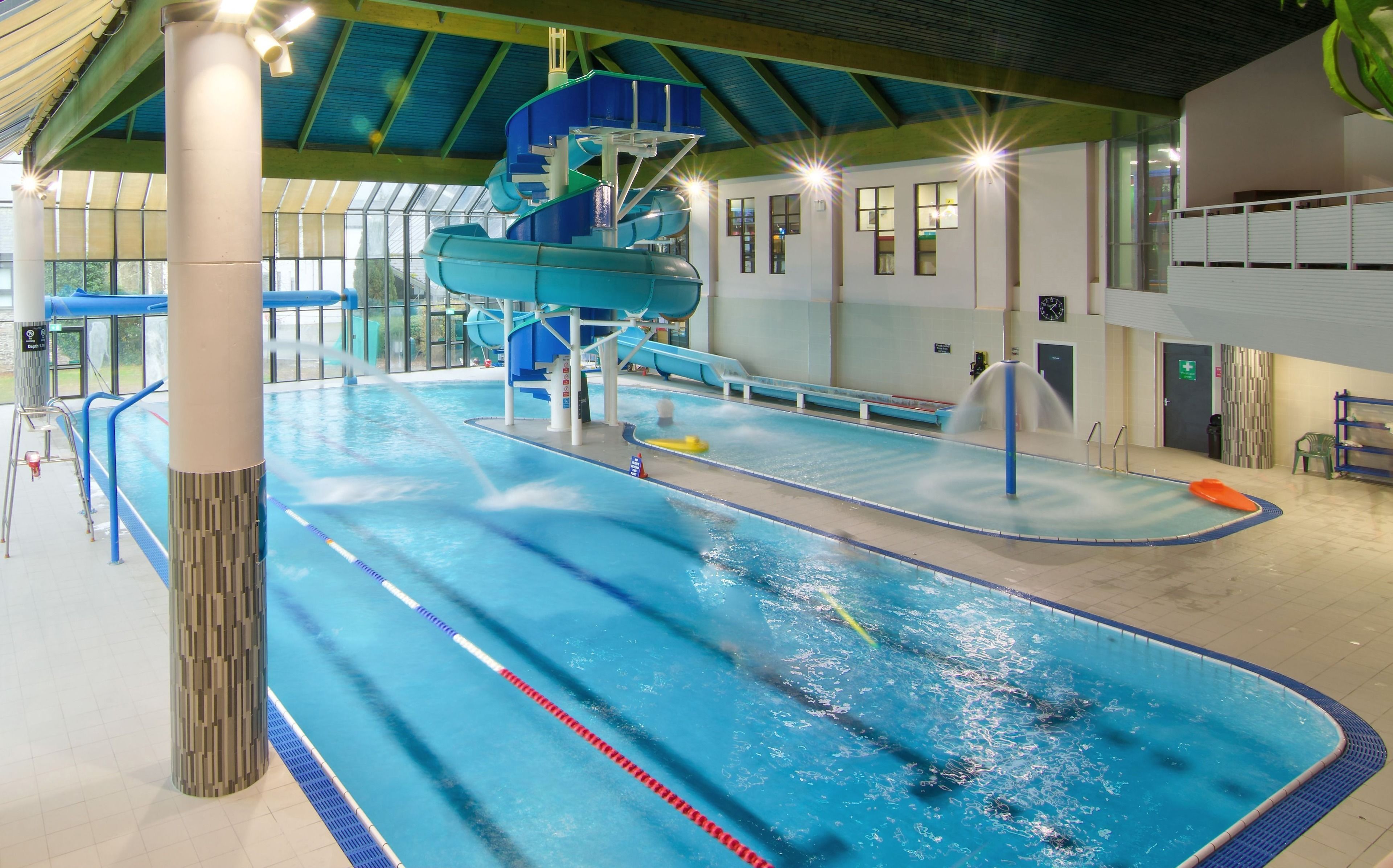 An indoor swimming pool with multiple lanes, a water slide, and a lifeguard stand.
