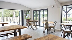 A modern dining area with wooden tables and metal chairs, large windows, and a view of the outdoors. - China Fleet Country Club (Saltash)