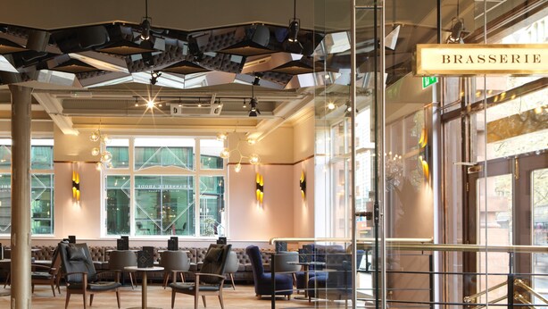 Un interno moderno con un'area salotto, una scala e un cartello con scritto 'BRASSERIE'.