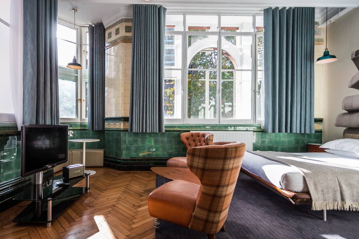 A hotel room with a large window, a television, a sofa, and a bed.
