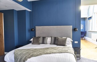 Un dormitorio moderno con una cama grande, paredes azules y un cabecero gris.