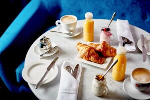 A breakfast setting with croissants, orange juice, coffee, and a jar of jam on a marble table.