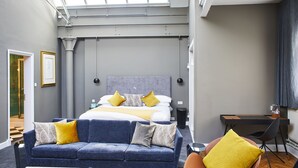 Una camera d'albergo moderna con un letto grande, un divano blu, una scrivania e vista sul cielo tramite un lucernario.