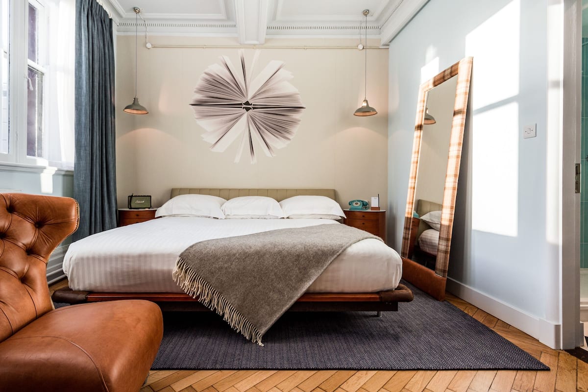 A bedroom with a large bed, a brown leather chair, a decorative wall piece, and a mirror.